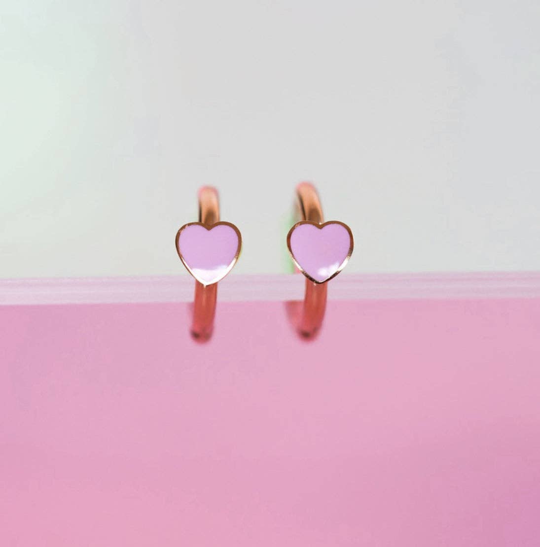Heart-shaped earrings with pink hearts on a light gray and pink gradient background