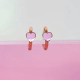 Heart-shaped earrings with pink hearts on a light gray and pink gradient background