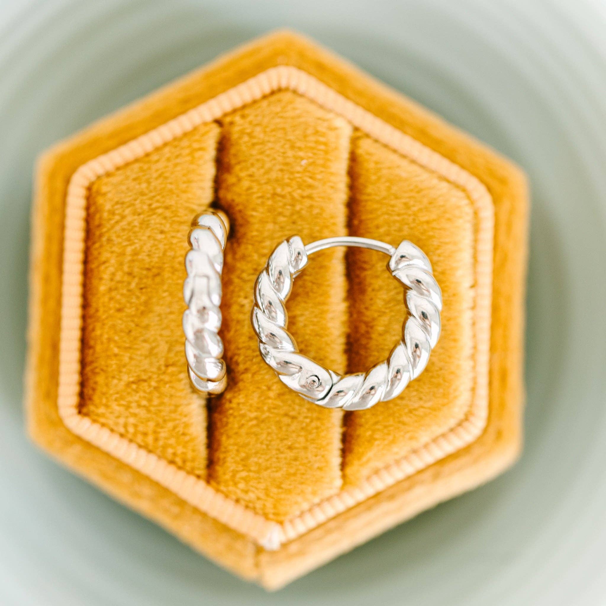 Two silver hoop rope earrings on a hexagonal yellow velvet cushion.