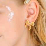 Gold bow-shaped earrings worn by a child with blonde hair.
