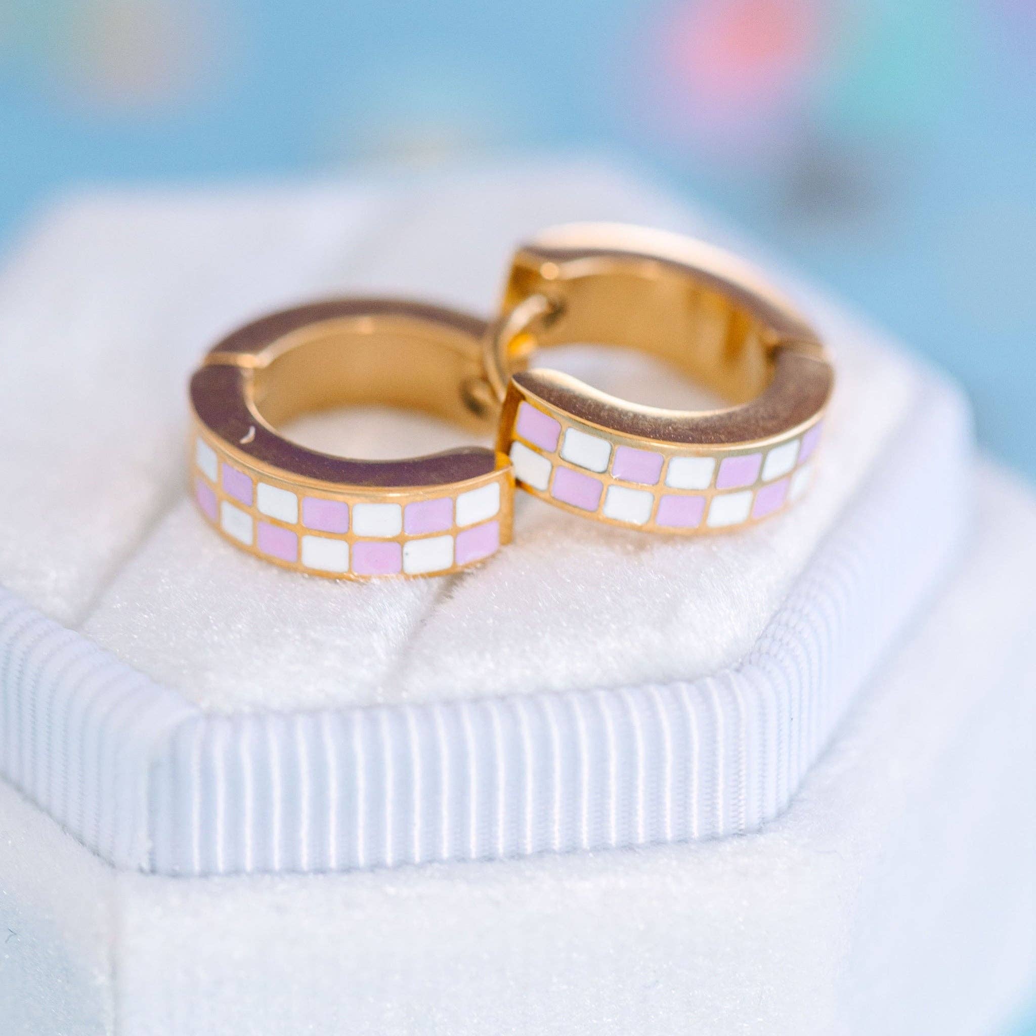 Gold hoop earrings with lilac and white checkered pattern on a light blue background