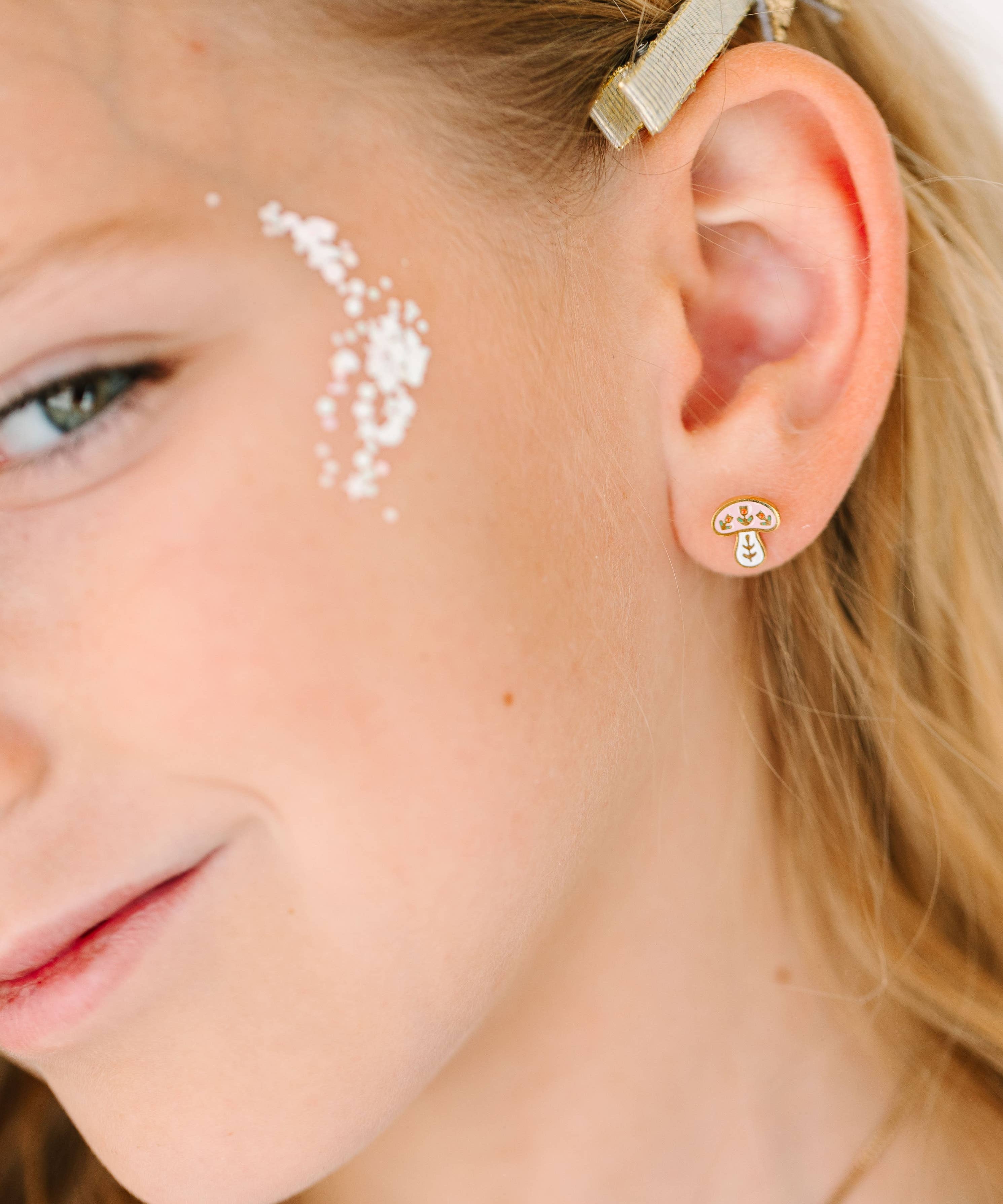 Close-up of a young girl wearing a gold mushroom earring with a winter mushroom design.