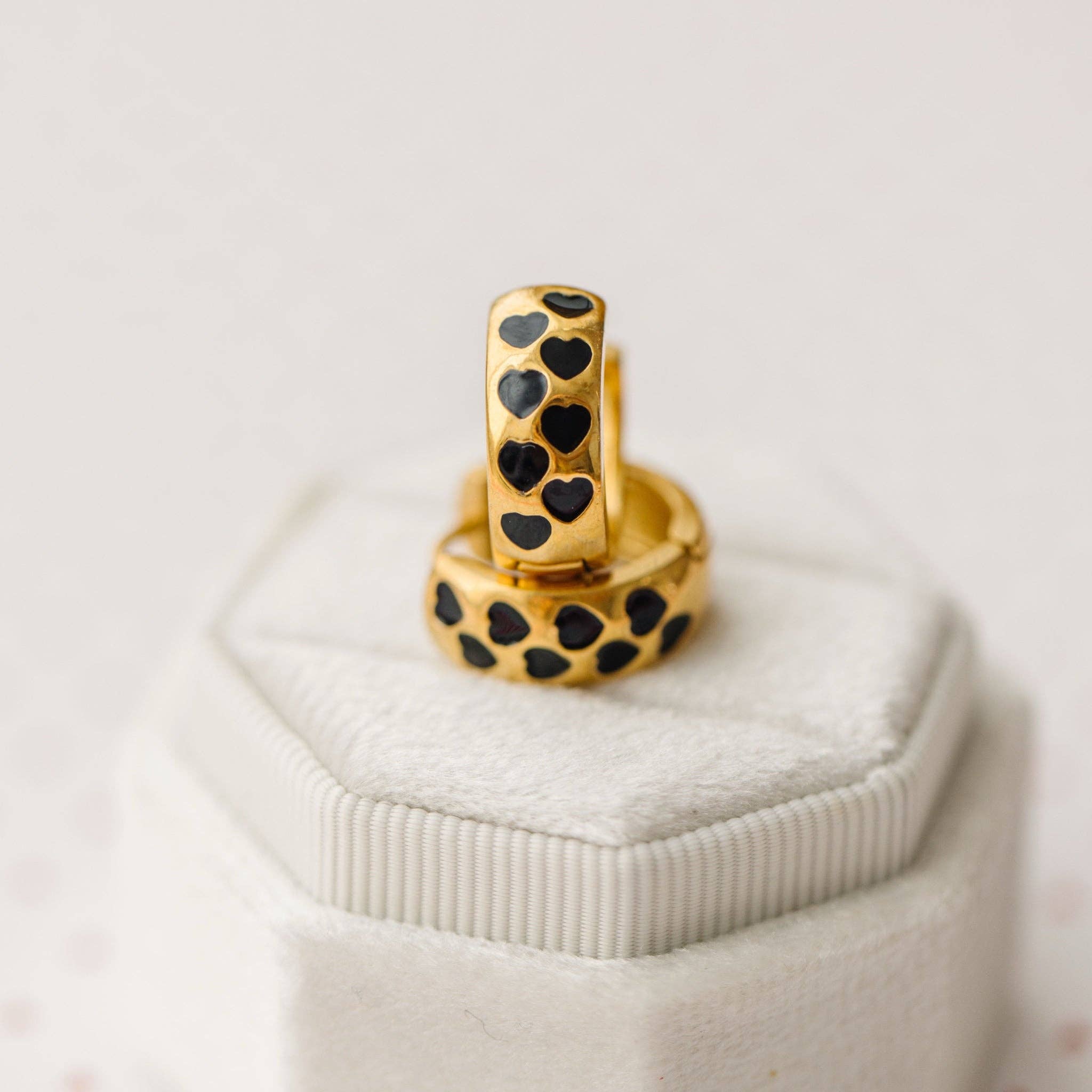 Gold earrings with black heart patterns on a white jewelry box