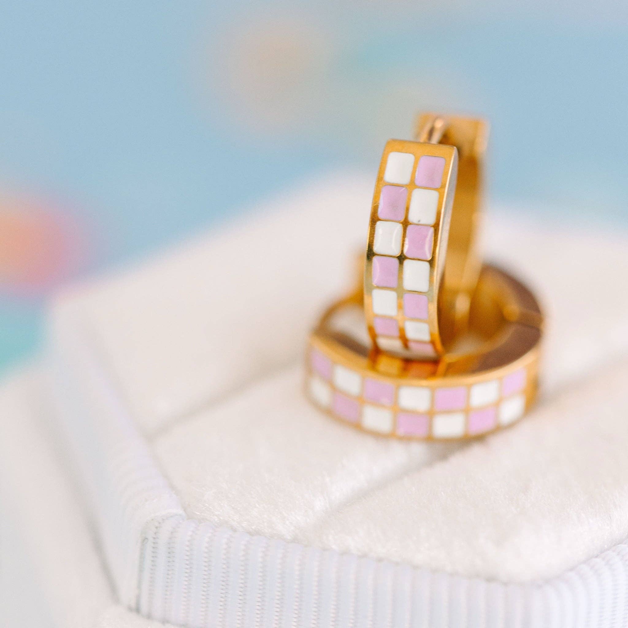 Two gold rings with lilac and white checkered pattern on a light fabric background