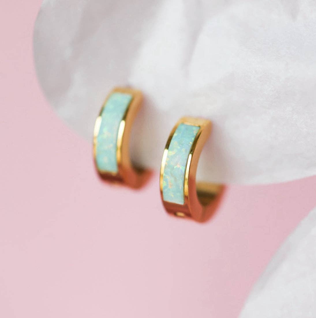 Gold hoop earrings with opal centers on a white surface with pink background