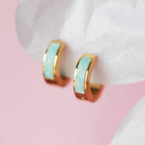 Gold hoop earrings with opal centers on a white surface with pink background
