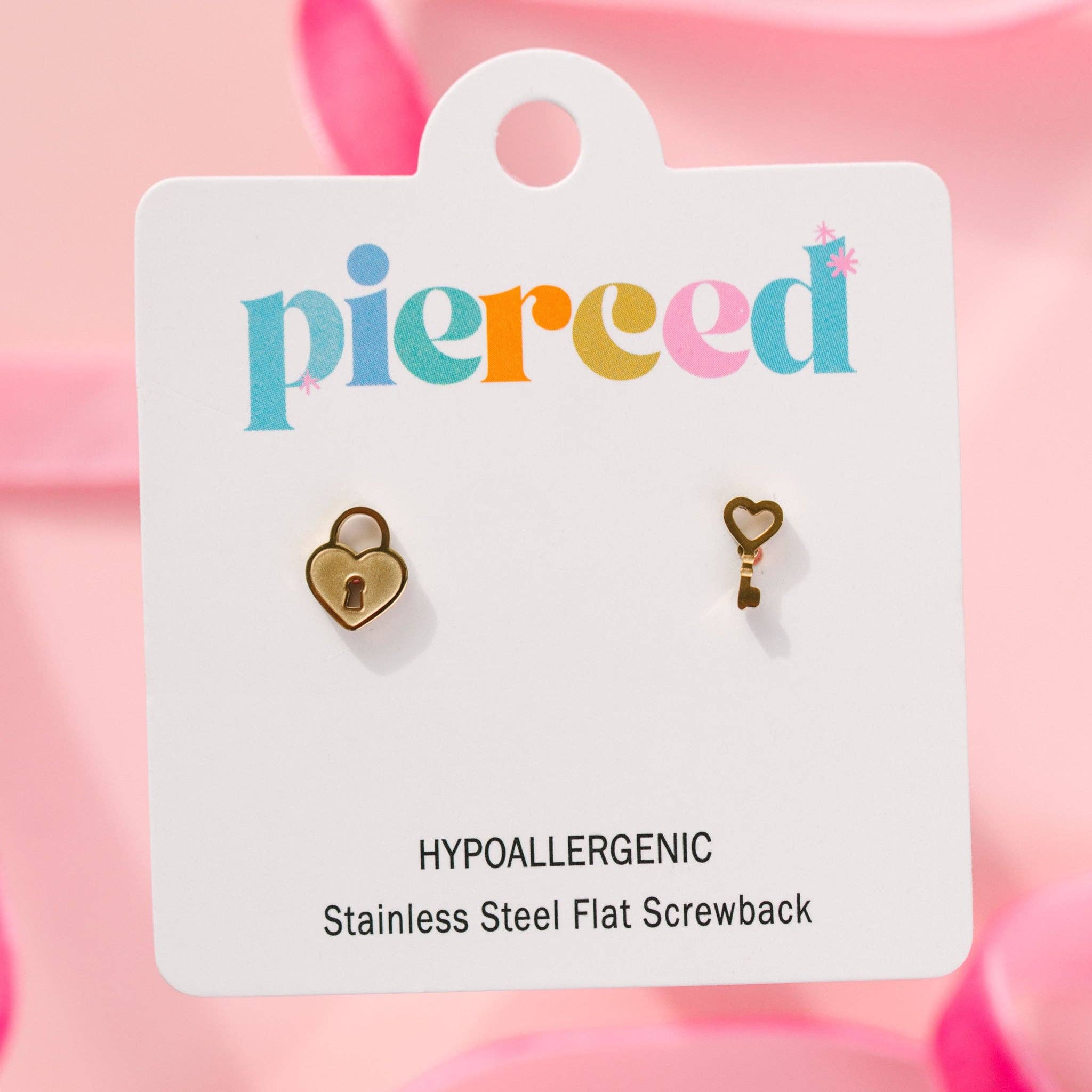 gold heart-shaped lock and key earrings  on a 'pierced' branded card with pink background