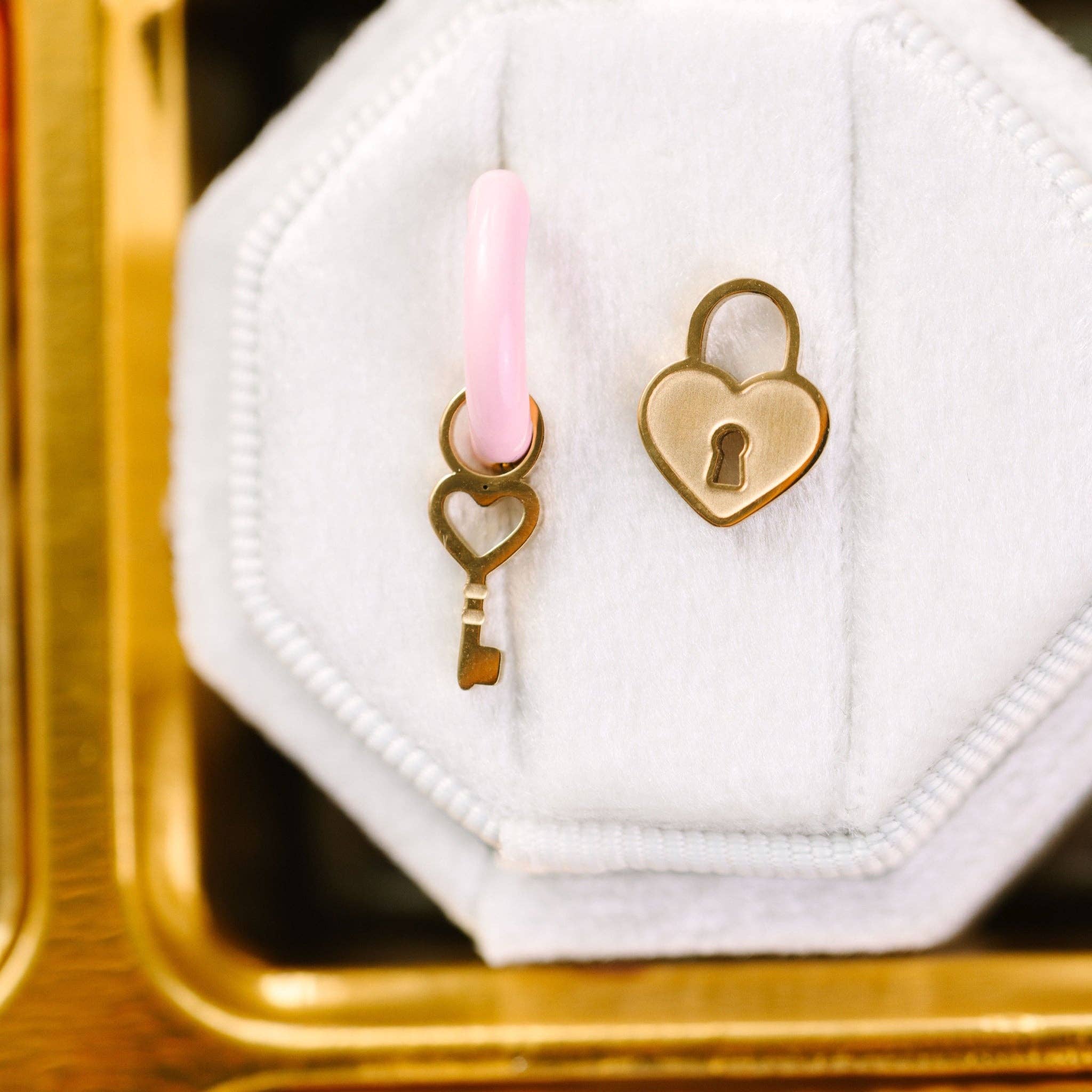Heart-shaped key and lock charms on a white hexagonal object with a pink candle in the background.