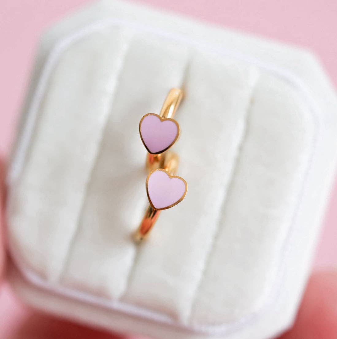 Gold earring with pink heart-shaped stones in a white box on a pink background