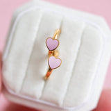 Gold earring with pink heart-shaped stones in a white box on a pink background
