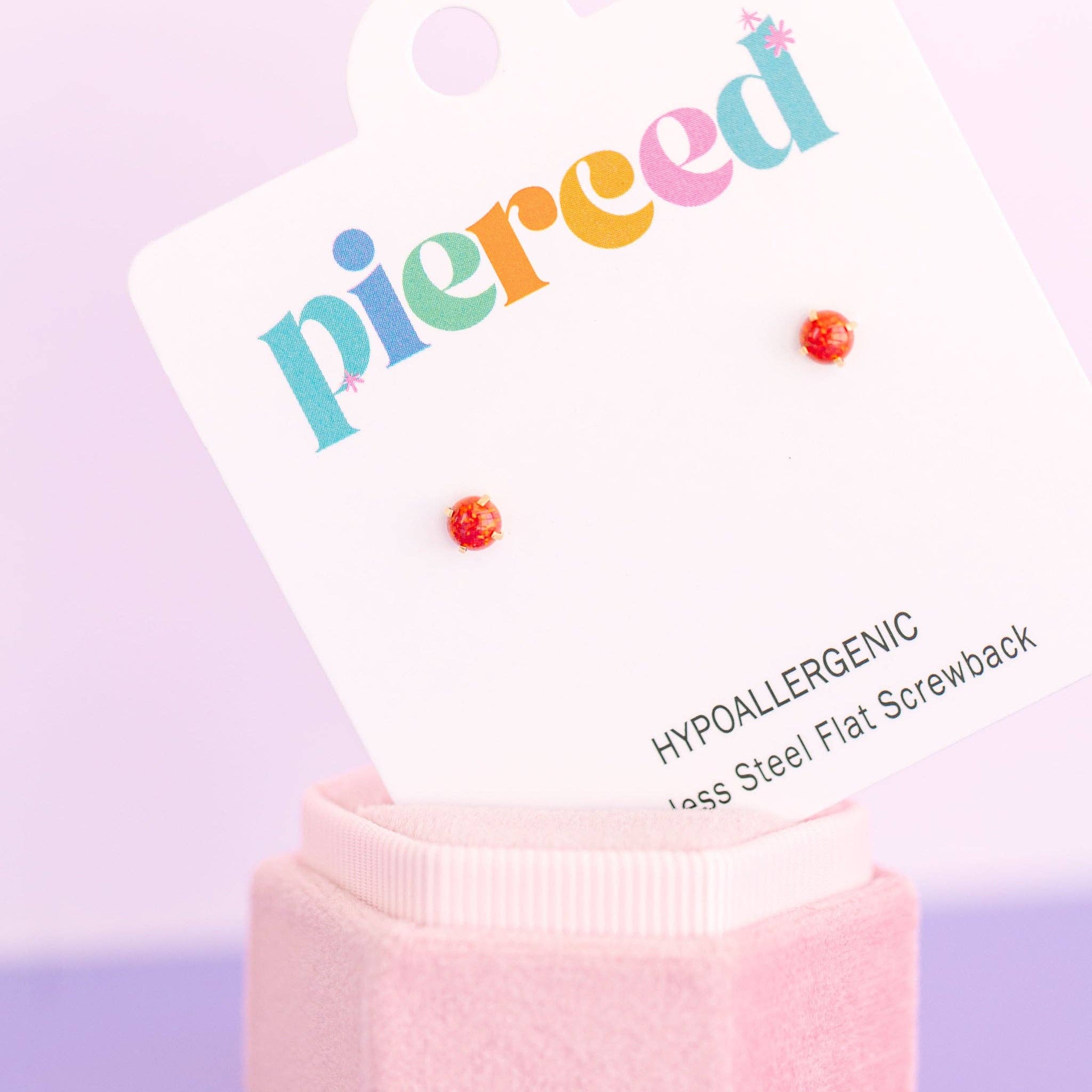 Earring display card with colorful 'pierceed' text and red earrings on a pink stand against a light purple background.