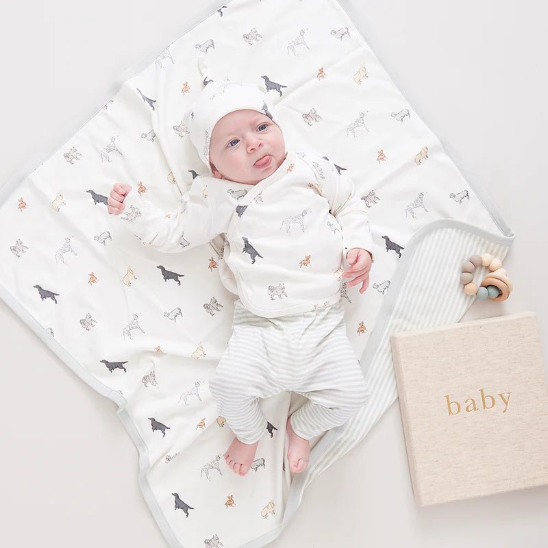 Baby dressed in dog and stripe print clothing laying on top of the dog print baby blanket