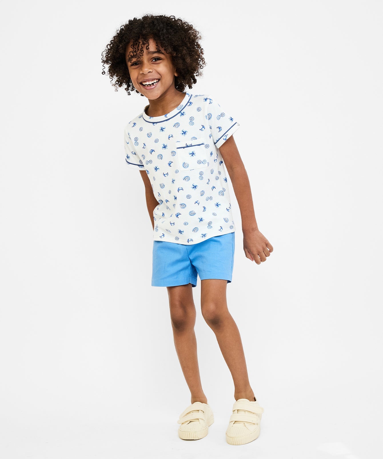 Child wearing a white t-shirt with blue floral pattern and blue shorts on a white background